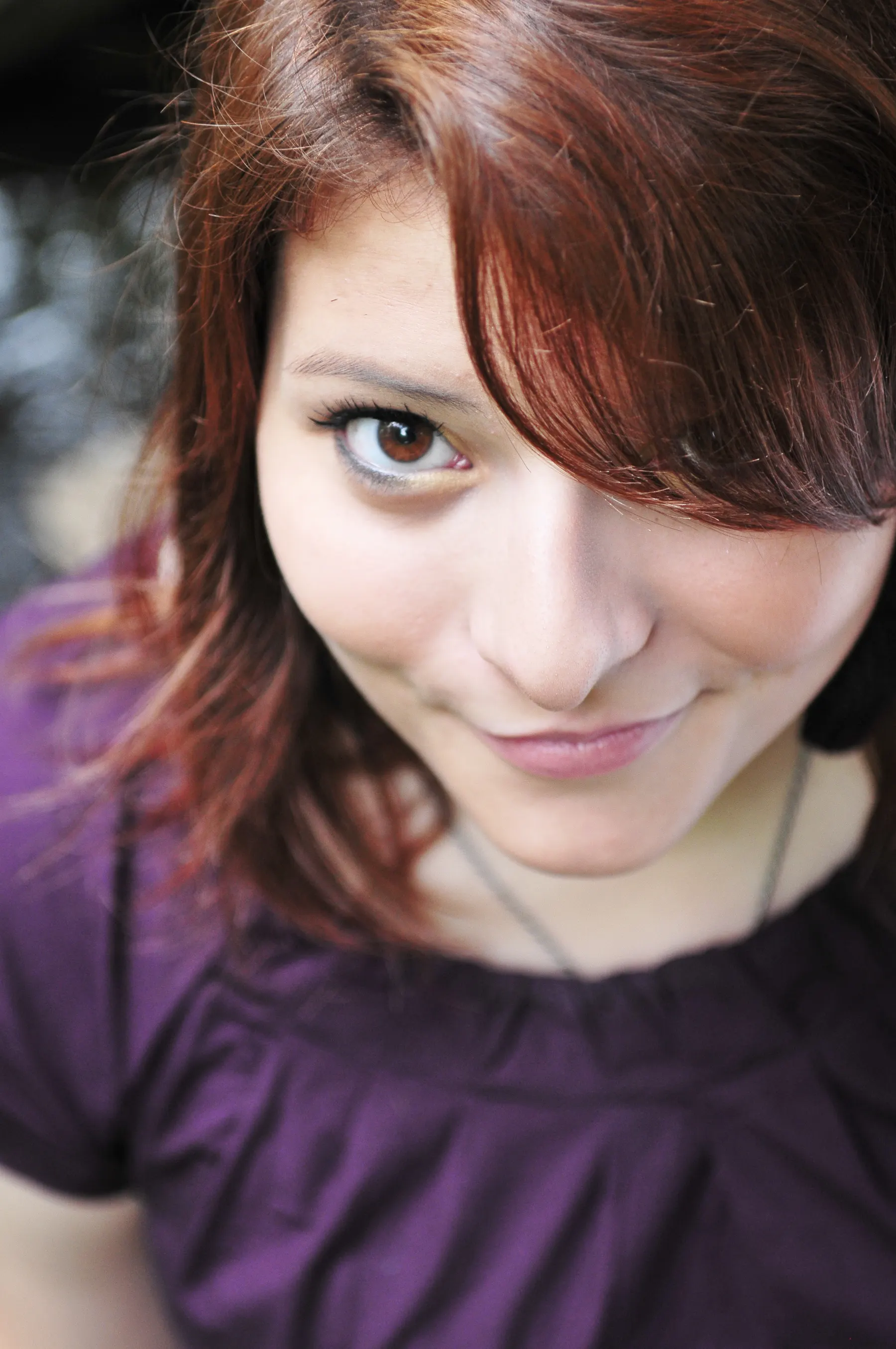 A close portrait of a senior with auburn hair and a purple top looking up at the camera
